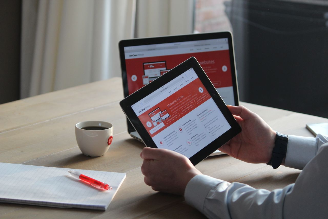 creative-01 Business professional using a tablet and laptop with a hot drink, focusing on digital content review.